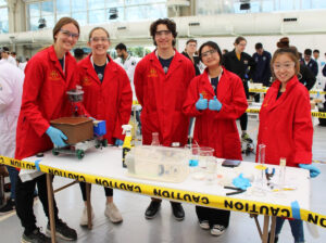 Members of the ISU chapter's Chem-E-Car team pictured in their lab coats and safety attire with their car in the competition's staging area